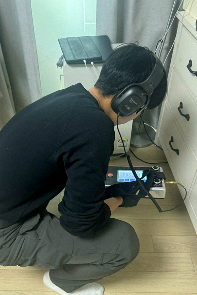 헤드폰을 쓰고 바닥에 청음 장비를 대어 소리를 듣는 작업 모습