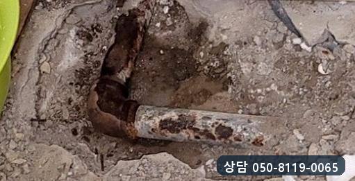 벽 쪽 바닥 속에서 드러난 녹슨 강관과 엘보 이음부