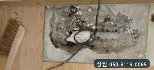 벽에 붙은 마루 바닥을 네모나게 걷어 낸 자리와 그 안의 배관