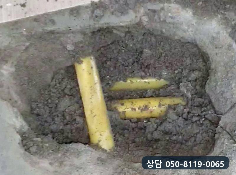 위층 바닥을 좁게 열자 젖은 흙 속으로 노란 배관이 드러난 모습