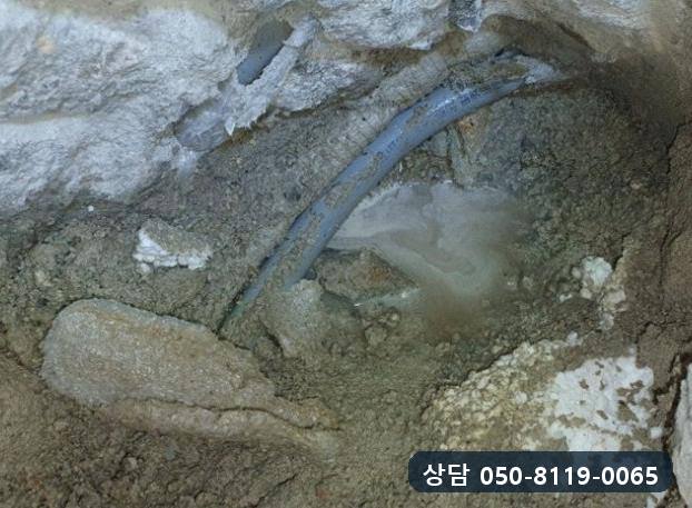 벽 밑에서 드러난 회색 온수관과 그 둘레에 고인 물