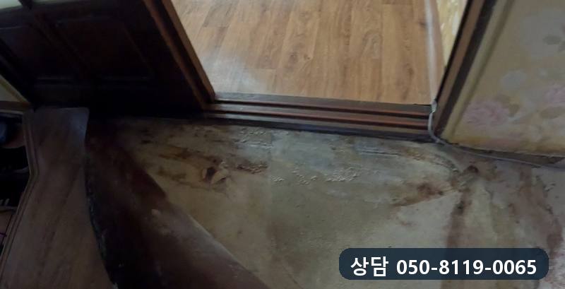 방문 문틀 아래 바닥이 넓게 젖어 얼룩진 모습
