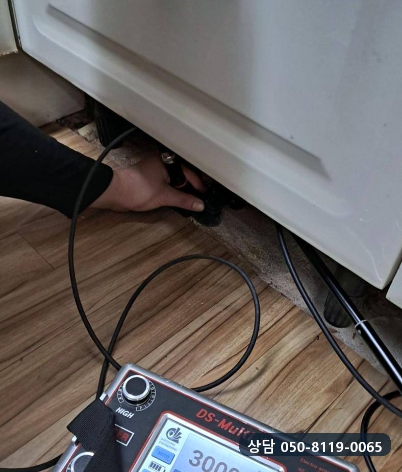 싱크대 아래 바닥에 감지기를 대고 본체 화면으로 수치를 확인하는 모습
